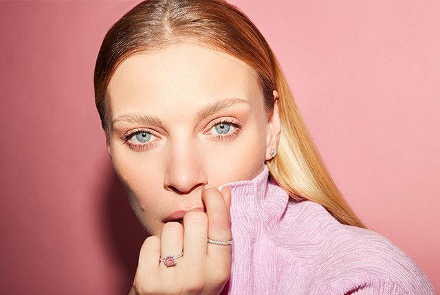 Woman wearing a rose gold diamond ring with a pink center stone and pavé band, plus a delicate stud earring