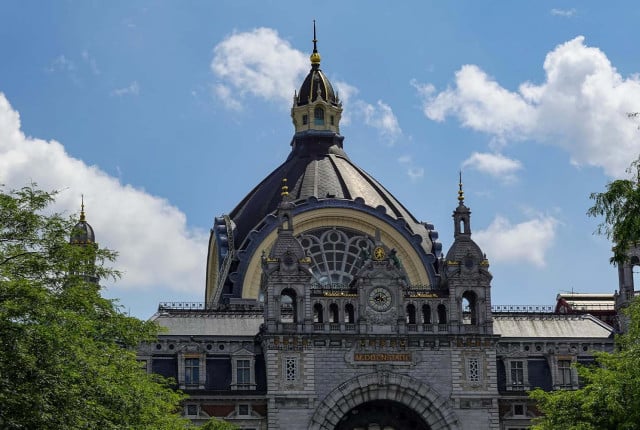 Historic Antwerp Central Station facade with ornate stone dome and clock beneath blue sky
