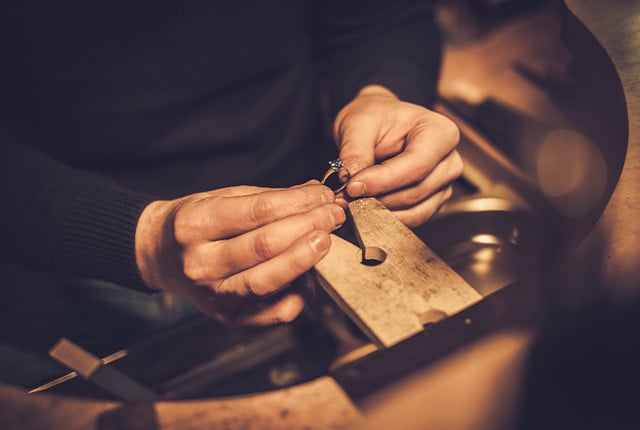 Joyería artesanal: manos de orfebre ajustando un anillo de metal con una pequeña gema en engaste fino.