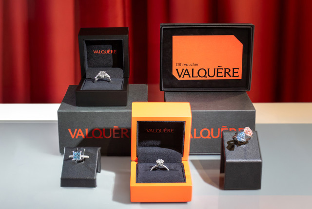 Tarjetas regalo Valquère junto a anillos de diamante en cajas negras y naranja sobre fondo rojo
