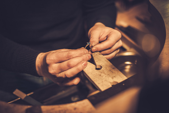 Artisan joaillier façonnant une bague en métal avec pierre sertie, sur établi en atelier.