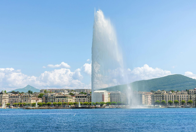 Veduta del Jet d’Eau a Ginevra sul lago, con skyline urbano e montagne sullo sfondo