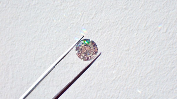 A sparkling lab-grown diamond with round cut held by diamond tweezers