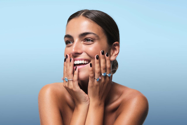 Vrouw met meerdere witgouden ringen met blauwe en roze diamanten in moderne zettingen
